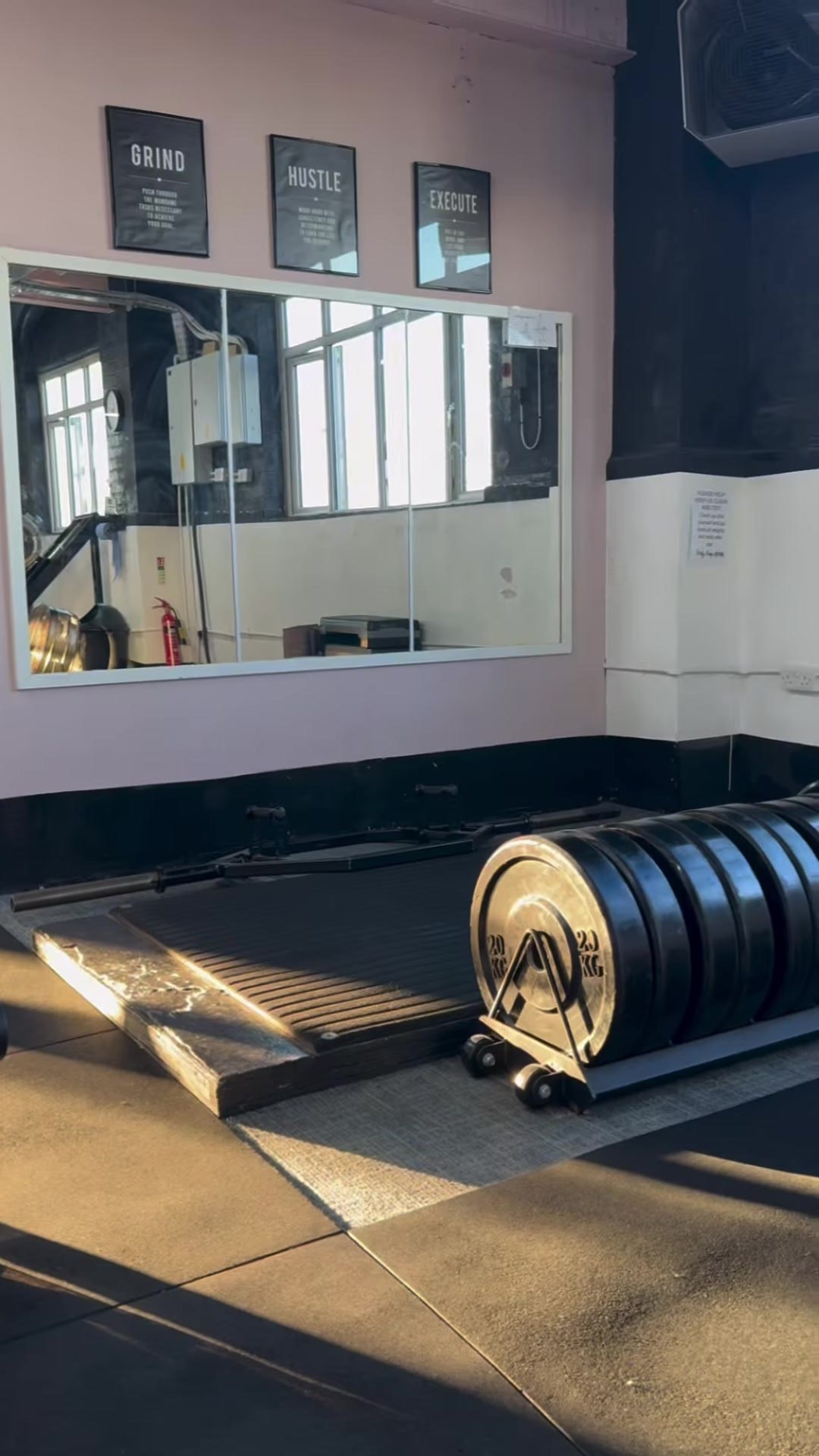 Lifting platform with bumper plates beneath a mirror and framed prints