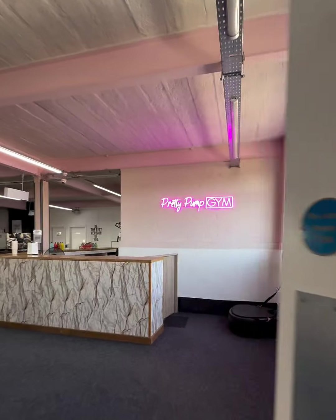 Reception desk with a pink Pretty Pump Gym neon sign on the wall